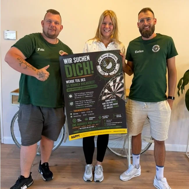 Drei Mitglieder des Dartclubs Rönner Breakfast mit ihrem Werbeplakat aus der 50×50-Plakataktion