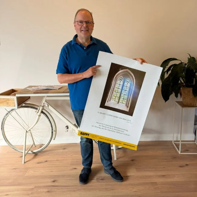 Mann hält ein A1-Plakat der evangelisch-lutherischen Kirchengemeinde Schönkirchen zur Wiedereinweihung – Teilnehmer der 50×50-Plakataktion